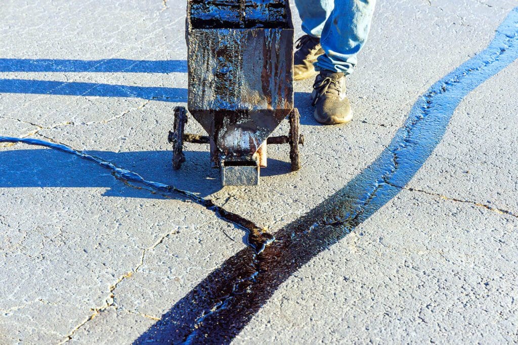 An asphalt patcher performs coated filling asphalt cracks sealing bitumen emulsion road surface restoration